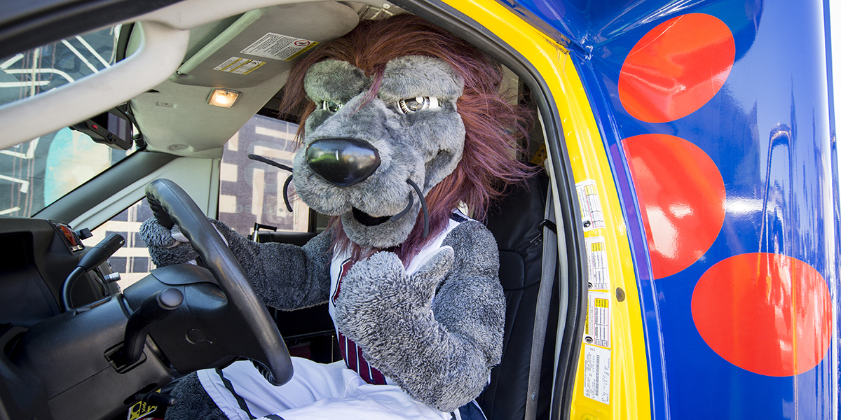 LMU mascot Iggy the Lion driving a shuttle bus.